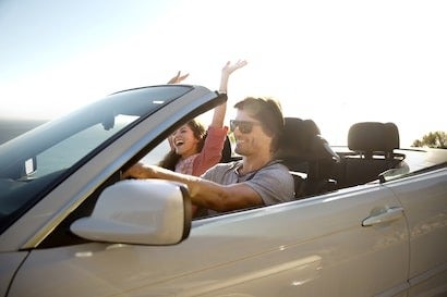 image of a couple riding in a convertable with a woman with her hands up